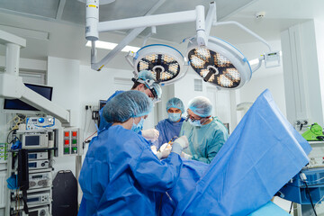 Surgeons in action in a modern hospital operating room. A team of surgeons conducts a complex...