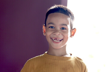Portrait of six year old Asian little boy in a yellow shirt smiling for showing false teeth. Joyful young kid child enjoys showing a happy expression.
