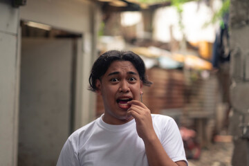 A young Filipino man with wide eyes, panicking and unsure of what to do. A local person living in a squatter settlement. Slum area background.