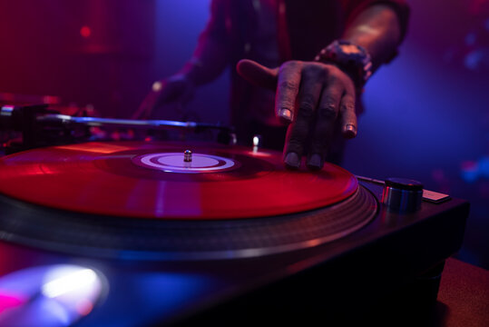 Hip hop dj scratching vinyl record on turntables against a black background in night club. Professional disc jockey plays music - Powered by Adobe