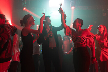 Friends at a disco to dance in celebration of new year at a social event with glasses of wine in hands