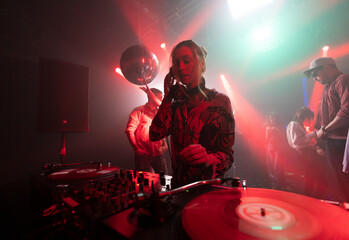 Professional female Dj in headset controlling the Dj turntable while a crowd of friends dancing...
