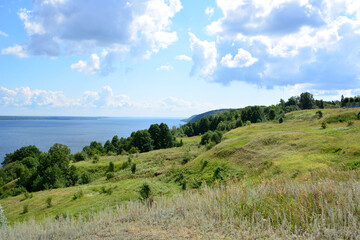 Naklejka premium a hilly coast with a view of a lake and trees and a cloudy sky