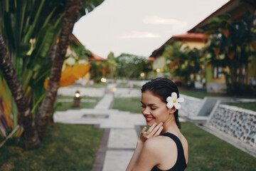 Woman with flower in her hair posing in front of tropical building with palm trees on sunny day