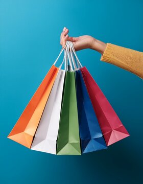 mano de mujer sujetando Bolsas de compras de colores  en un fondo azul de estudio