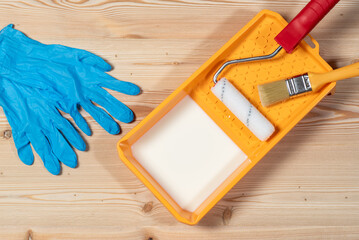 Tray with white liquid wax-oil for wood, brush, roller and gloves on a wooden background, before painting
