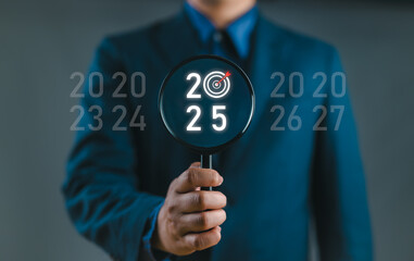 2025 and dartboard with arrow inside of magnifier glass on dark background for focus in new...
