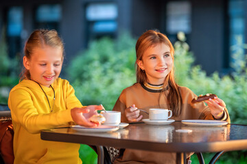 Two schoolgirls are sitting at a table in a city open-air cafe.