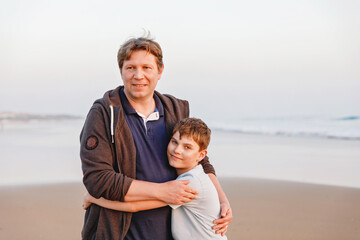 Healthy loving father and son together at the beach at sunset Happy family, love. Preteen boy and middle-aged man hugging. Happy relationship between parents and children.