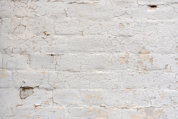 Weathered, aged brick wall, plastered, painted in cream, paintwork cracking and peeling