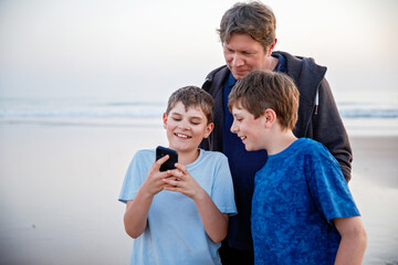 Healthy loving father and two boys together at the beach at sunset Happy family, love. Preteen sons and middle-aged man looking on smartphone. Happy relationship between parents and children.