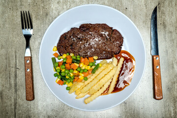 A plate of food with a piece of picanha meat, vegetable mix, and french fries with a sauce on the side