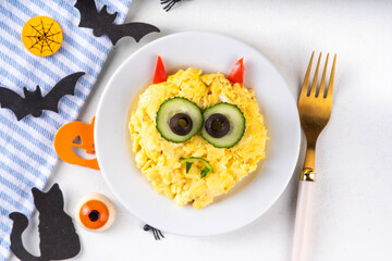 Halloween breakfast scrambled eggs shaped and decorated like cute monster, with fresh vegetables, funny kids Halloween food simple recipe idea
