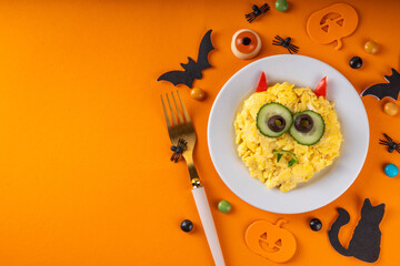 Halloween breakfast scrambled eggs shaped and decorated like cute monster, with fresh vegetables,...
