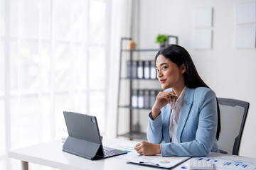 A woman in a blue suit is sitting at a desk with a laptop and a tablet