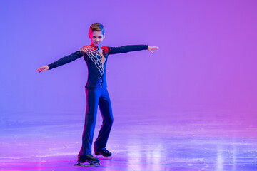 Boy figure skater skating on ice. With festive colored lilac lighting. © Maria Moroz
