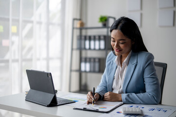 A woman in a blue suit is sitting at a desk with a laptop and a notepad