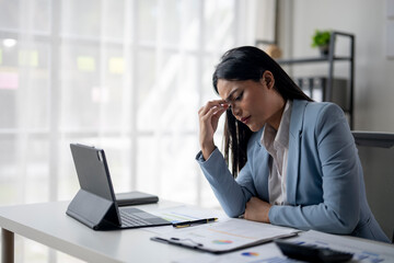 Fototapeta premium A woman in a blue suit is sitting at a desk with a laptop and a stack of papers
