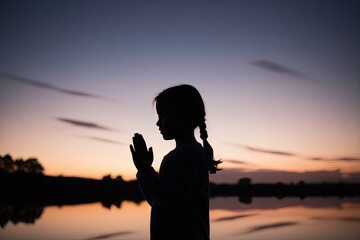 Fototapeta premium Twilight Silhouette of a Young Girl Praying Reflecting Harmony and Spirituality