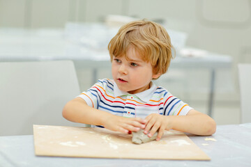 Little blond boy modeling with clay at master class art in a museum, indoors. Creative leisure for kids in kindergarden and at home, indoors.