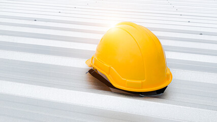 Features a bright yellow safety helmet resting on a clean metal roof, bathed in sunlight, highlighting safety in construction environments. Perfect for representing industry, safety protocols.