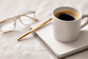 A warm cup of coffee sits next to a notebook and glasses, inviting a peaceful morning vibe perfect for reflection and planning the day ahead