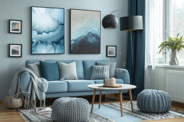 Scandinavian-style living room featuring a blue armchair, grey sofa, knitted ottomans, abstract art paintings, and a black floor lamp, with soft lighting creating an inviting atmosphere.