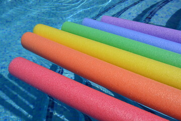 Colourful swim noodles float on swimming pool