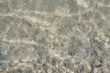 Blurred water surface with transparent ripples and visible rocks at the bottom, creating a serene, natural background effect