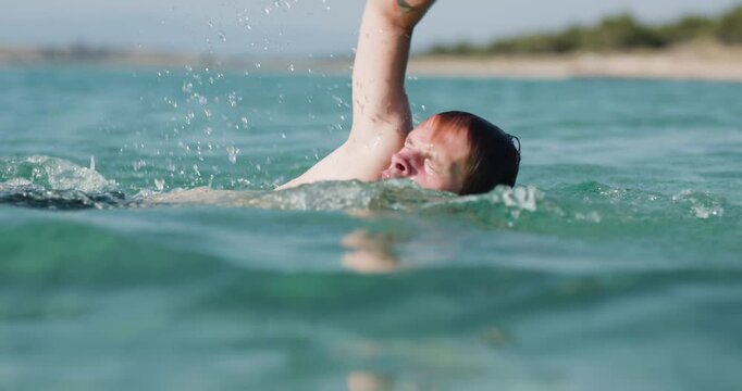 Man swimming energetically in the sea, splashing water around. Recorded at 120 fps on cinema camera.