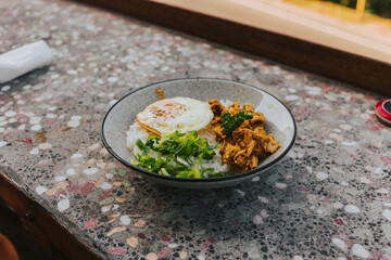 Rice with fried egg and vegetables in a round ceramic plate on the countertop. Asian Lunch Concept