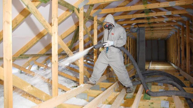 Man with a hose is spraying cellulose insulation in the attic of a house