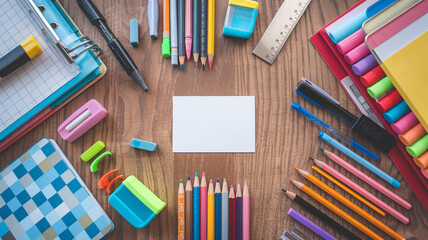 Obraz premium School supplies on wooden table, background with frame made of stationery and blank paper card in center.