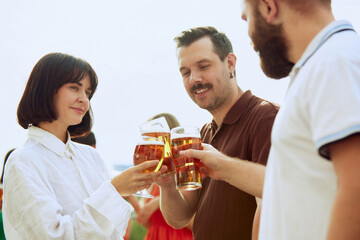 Group of friends clinking beer glasses, celebrating their meeting outdoor. Young people looks happy and cheerful. Concept of Friday mood, celebration, lunch break and Oktoberfest.