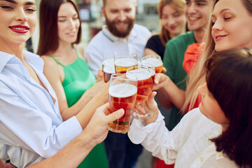 Group of friends toasting, cheering, clinking glasses of cold lager beer, on Oktoberfest festival. Celebration outdoor. Concept of Friday mood, celebration, lunch break and Oktoberfest.