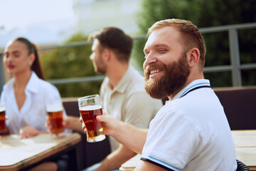 Group portrait of friends sitting at terrace talking, drinking alcohol, celebrating meeting after long years. Festive atmosphere. Concept of Friday mood, celebration, lunch break and Oktoberfest.