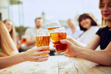 Friends raise their glasses in joyful toast, enjoying sunny day outdoors. Golden drinks glisten in light, capturing spirit of celebration. Concept of Friday mood, celebration, Oktoberfest.