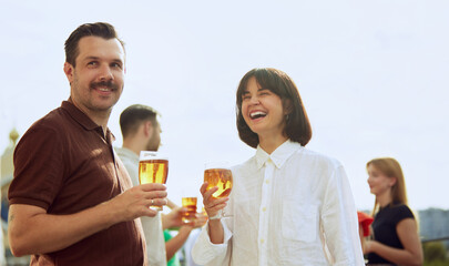Man and woman enjoy beautiful sunny day, talking and relaxing, drinking beer on sunlit terrace. Festive atmosphere. Concept of Friday mood, celebration, lunch break and Oktoberfest.