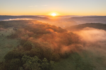 Aerial scene above the forest on Via Transilvanica. Foggy landscape above the green oak trees	
