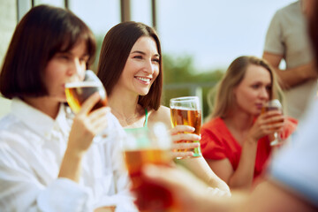 Joyful group enjoys cold beers on terrace, clinking glasses and smiling, celebrating friendship and simple pleasures of life. Concept of Friday mood, celebration, lunch break and Oktoberfest.