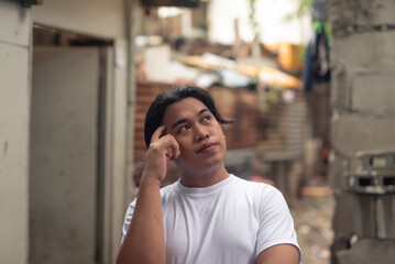 A young asian man ruminating thinking of ways to solve his current problems. Slum area background.