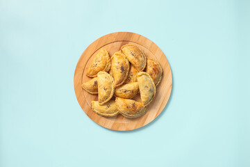 Top view baked samsa pies with chicken sprinkled with poppy seeds on wooden plate on blue background.