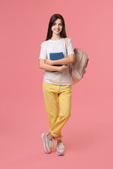 Fototapeta premium Cute teenage girl with backpack and books on pink background