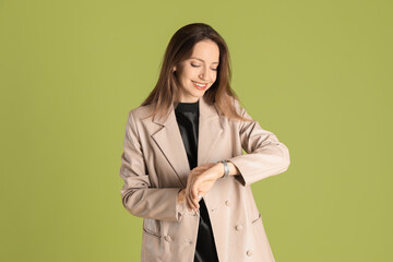 Beautiful woman in stylish beige jacket checking time on olive background