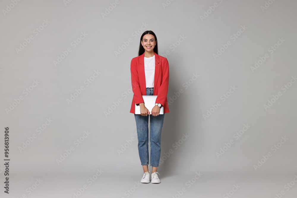 Canvas Prints Beautiful woman in red jacket with laptop on gray background