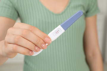 Woman holding positive pregnancy test indoors, closeup view