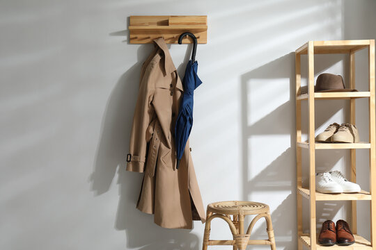 Colorful umbrella and trench coat hanging on rack at home