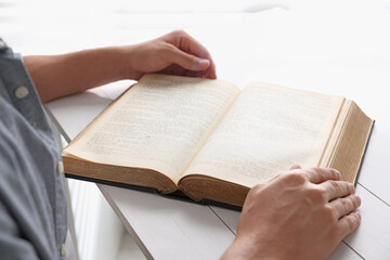 Naklejka premium Man with Bible at white wooden table, closeup