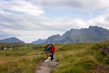 Happy children with parents and dog, european family, hiking the Kvalvika trail on hill at Kvalvika beach, Norway