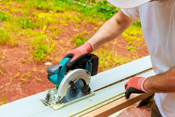 Working with circular handsaw, worker cuts plastic vinyl siding to required size before installing it